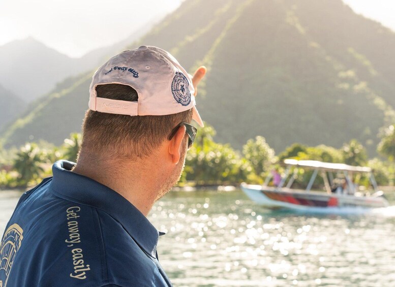 A person wearing a cap and a blue shirt with 'Get away, easily' text, looking at a boat on water with mountains in the background. 3