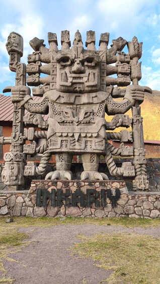 A large stone sculpture with intricate carvings, a sign reading 'INAHARU,' and a mountainous background. 1