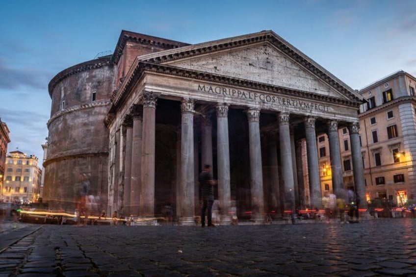 A classical building with columns and inscriptions, surrounded by cobblestone streets and other historic architecture. 2
