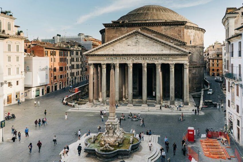 A historic building with columns and a dome, surrounded by a plaza with a fountain and people. 1