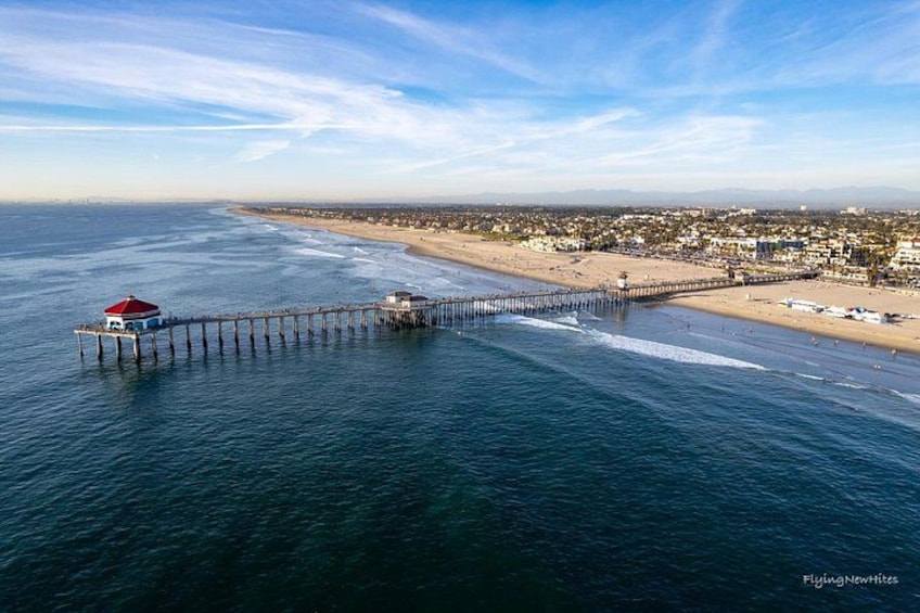 A pier extending into the ocean with a red-roofed structure at the end, a beach, and a distant cityscape. 2