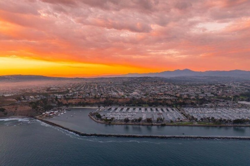 A coastal cityscape at sunset with a marina and a large parking area. 4
