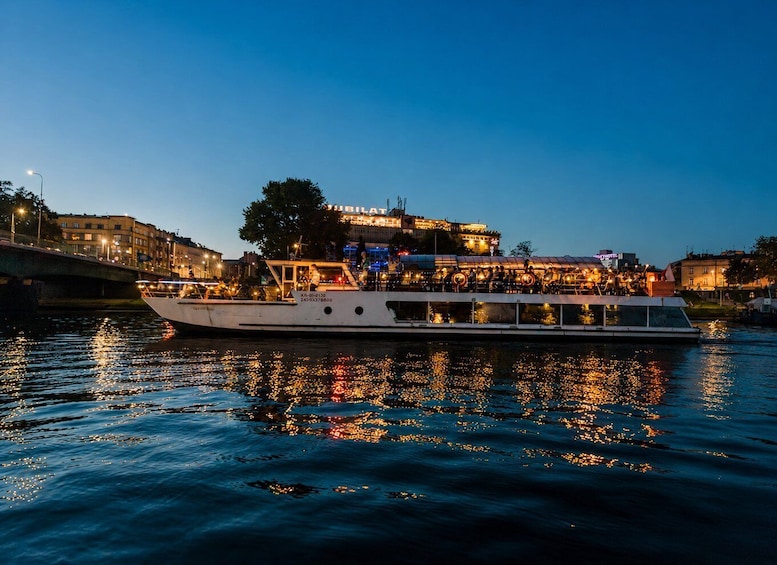 A riverboat with passengers, docked near a cityscape with illuminated buildings at dusk. 2
