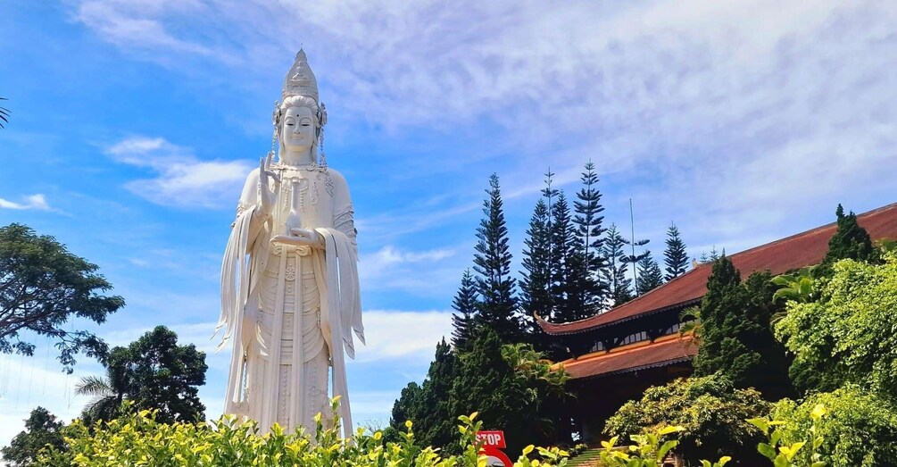 Eine große weiße Statue, ein traditionelles Gebäude und ein bewaldetes Gebiet. 1