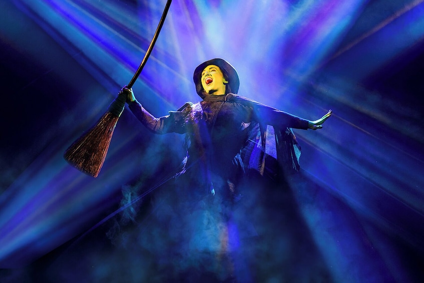 A person in a dark costume with a broom, surrounded by blue light effects. 2
