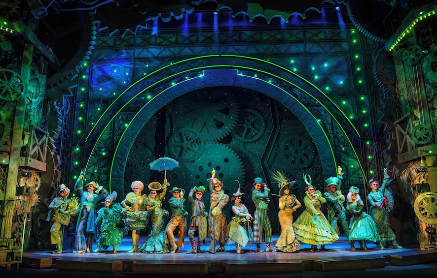 A theatrical stage with performers in period costumes, a large arch structure, and mechanical gears. 3