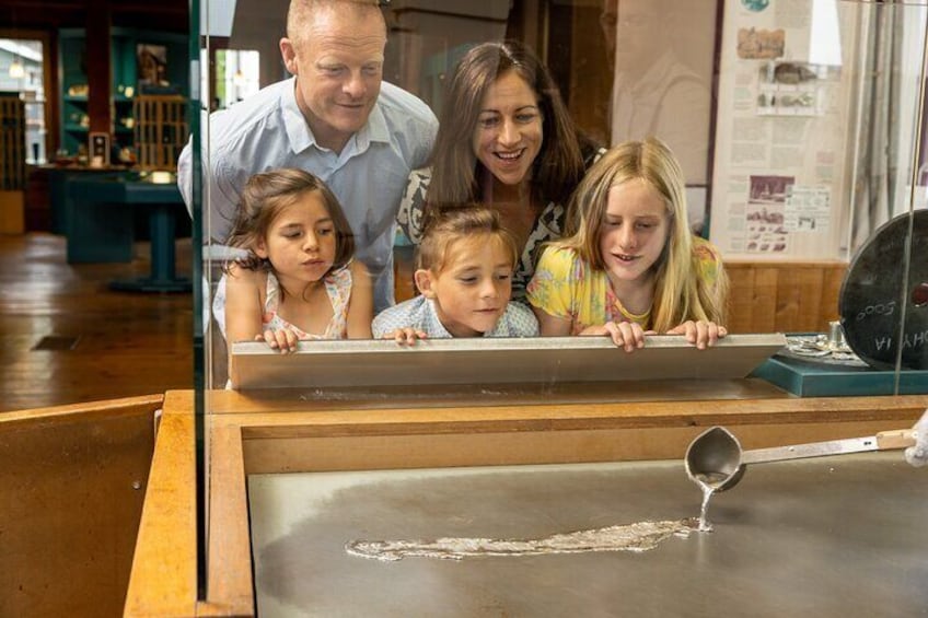 A family observing a metal object on a display table in a museum. 2