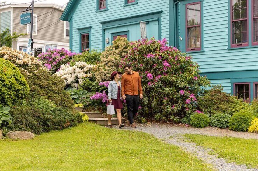 A turquoise house with a garden, a man and a woman standing in front, and a street sign in the background. 4