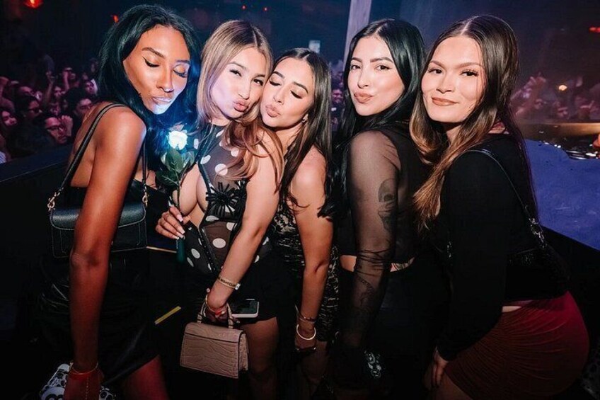A group of people at a social event, likely a party or club, with dim lighting and a crowd in the background. 4