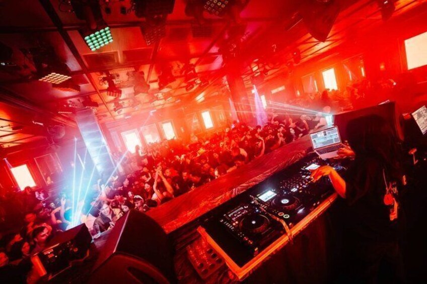 A crowded club with a DJ booth and red lighting. 3