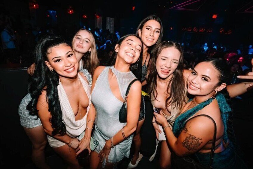 A group of people at a social event, likely a party or club, with a dimly lit background and a crowd. 2