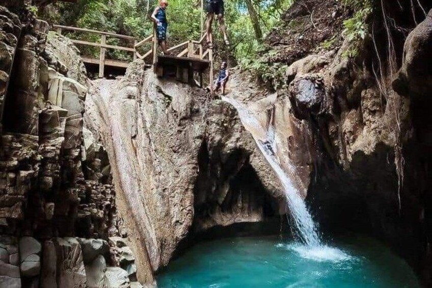 A waterfall in a rocky gorge with a wooden bridge and a pool at the base. 2