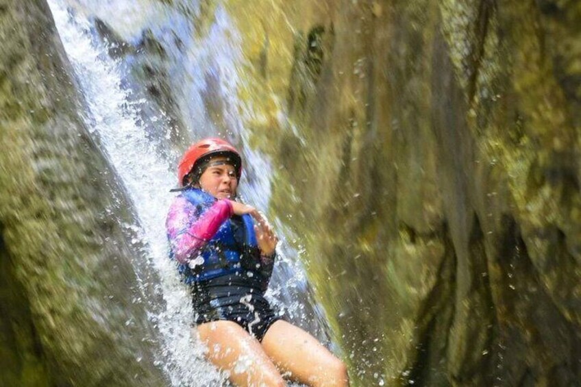 A person in a blue and pink jacket and red helmet navigating a narrow water channel. 1