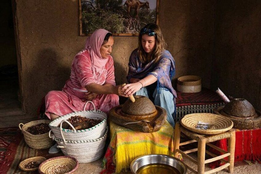 Two women sitting on a colorful rug, surrounded by baskets and containers, likely involved in a traditional activity. 1
