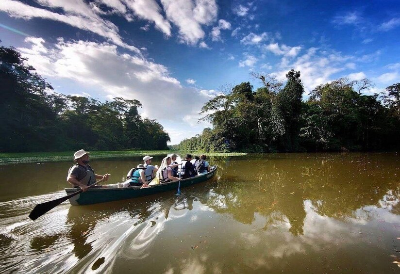 A group of people in a canoe on a calm river, surrounded by lush greenery. 3