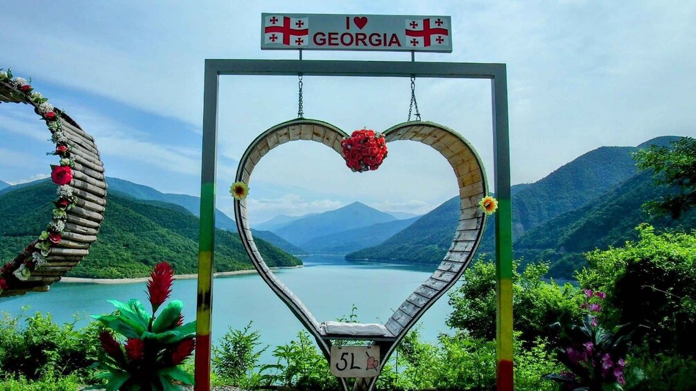 A heart-shaped archway with a Georgia flag sign above it, overlooking a lake with mountains in the background. 3