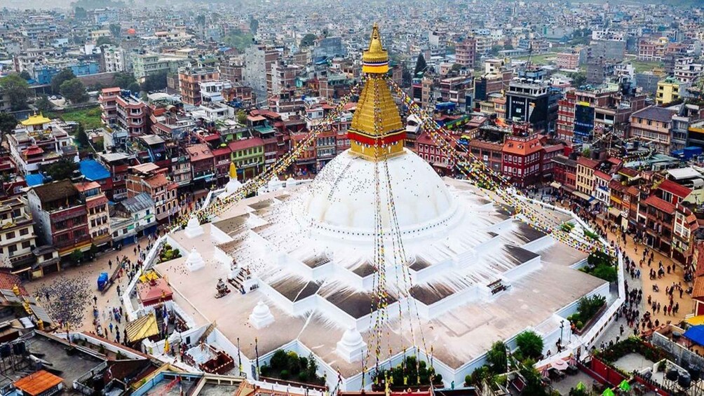 A large white stupa with a golden spire surrounded by a crowd in a cityscape. 4