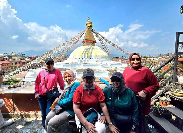 A group of people on a rooftop with a large golden dome and colorful prayer flags in the background. 1