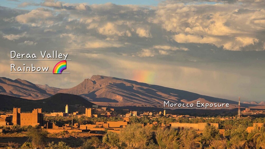 Eine Wüstenlandschaft mit Bergen, einer Stadt und einem Regenbogen. 4