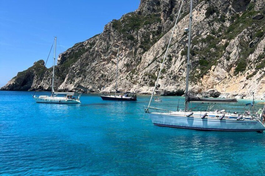 A calm sea with boats anchored near rocky cliffs. 4