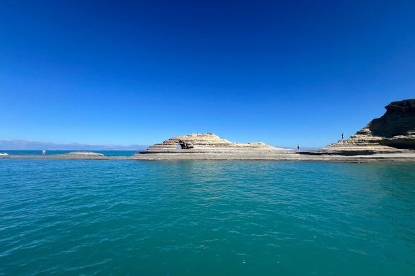 A coastal landscape with clear blue waters, a rocky outcrop, and a distant lighthouse. 3