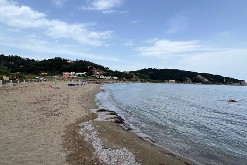 A sandy beach with gentle waves, a clear sky, and a hilly landscape in the background. 2