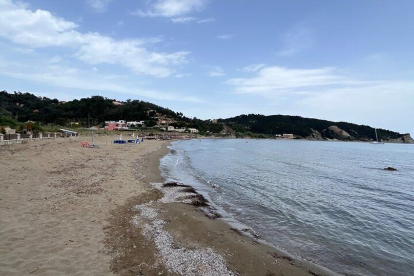 A sandy beach with gentle waves, a clear sky, and a hilly landscape in the background. 2