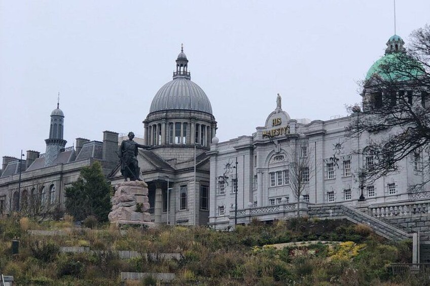 A large historical building with a dome and a statue in front. 1