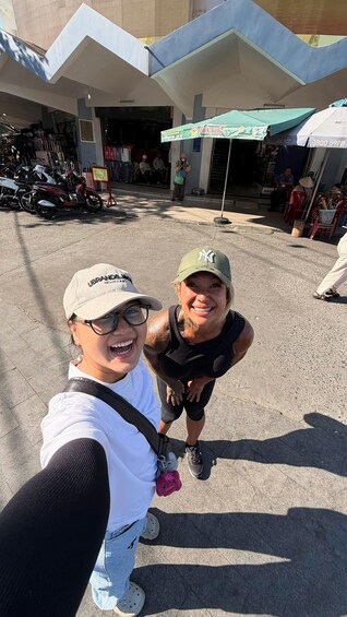 Two people taking a selfie in an outdoor market area with motorcycles parked in the background and a storefront with a green awning. 3