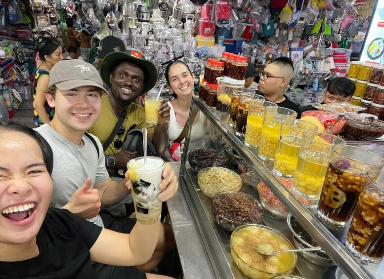 A group of people at a beverage stand with various drinks and snacks. 1