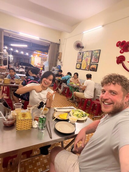 A group of people dining inside a restaurant with tables, chairs, and various food items on the tables. 5