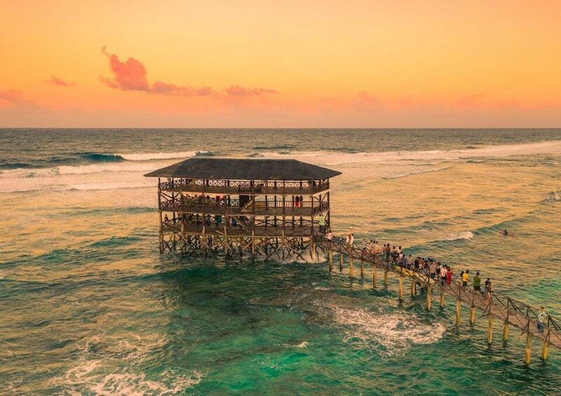 A wooden pier extending into the ocean with a covered structure at the end, surrounded by clear turquoise water. 2