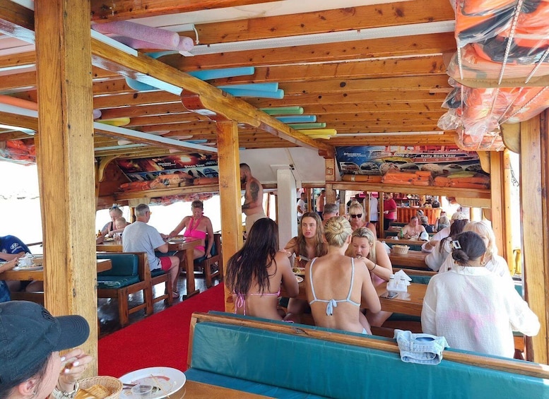 A wooden boat deck with people dining and a sign for a daily boat tour. 3
