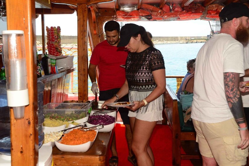 A buffet setup with various food dishes on a wooden table, a person serving food, and a body of water in the background. 1
