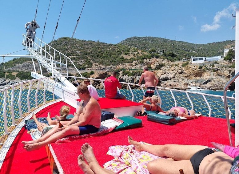 People sunbathing on a boat deck with a red carpet, surrounded by rocky terrain and hills. 2
