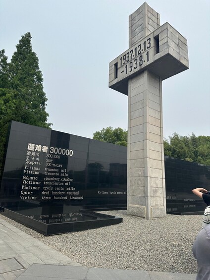 A memorial monument with inscriptions in multiple languages, surrounded by gravel and trees. 1