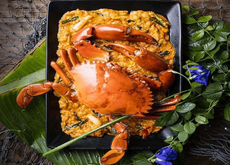 A crab on a plate with a yellowish dish, surrounded by green leaves and blue flowers. 2