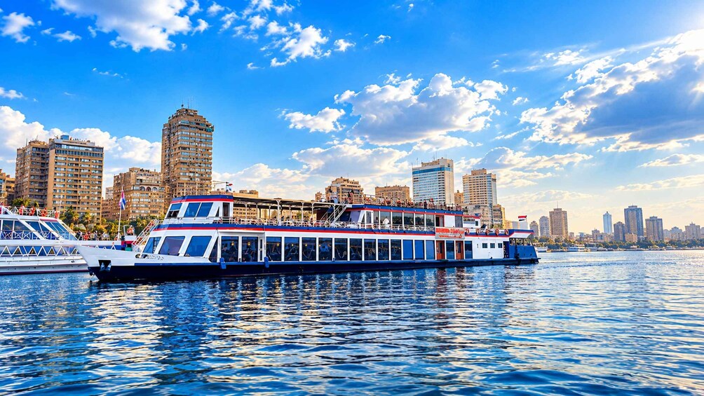 Un bateau de croisière naviguant sur une rivière, avec la silhouette d’une ville en arrière-plan. 1