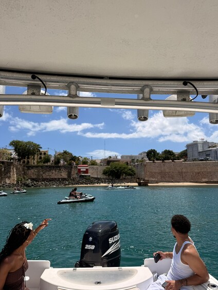 A boat with a Suzuki outboard motor, a person pointing towards the shore, and a coastal landscape with buildings and a stone wall. 5