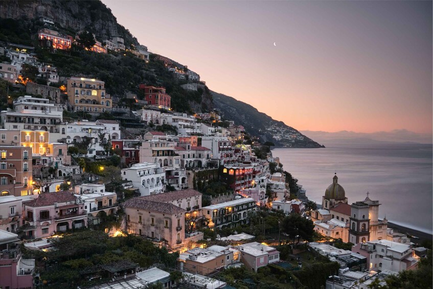 A coastal town at dusk with buildings along the hillside and a church with a dome. 5