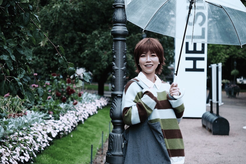A person holding an umbrella, standing next to a lamppost in a garden with flowers and a sign that reads 'HELLO'. 4