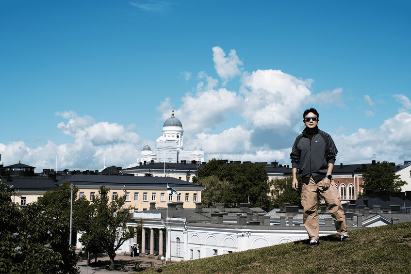 A person standing on a grassy hill with a cityscape in the background, including a prominent white building with a dome. 3