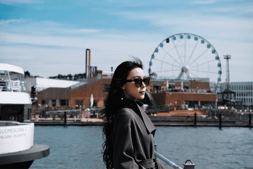 A person standing by a waterfront with a Ferris wheel and industrial buildings in the background. 2