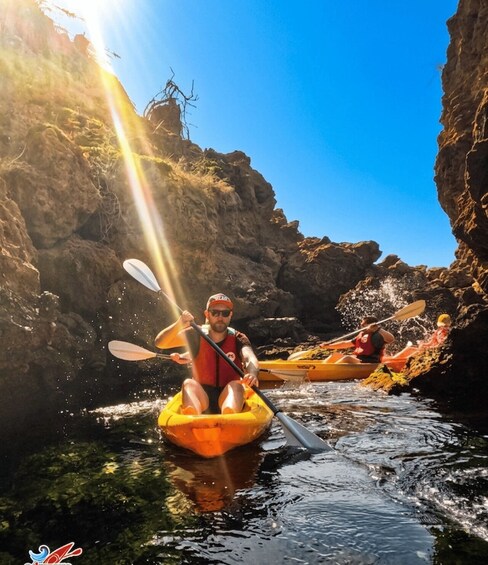 Two people kayaking in a narrow water channel surrounded by rocky cliffs. 2