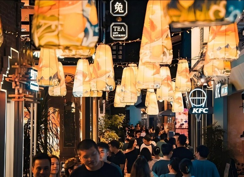 A crowded street at night with hanging paper lanterns and illuminated signs for a tea shop and KFC. 3