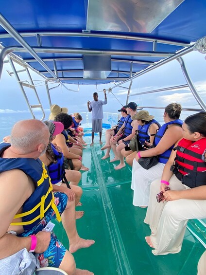 A group of people on a boat, some wearing life jackets, with a man speaking to them. 4