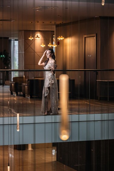 A woman in a dress standing on a balcony with a railing, in a modern building with hanging lights and a door labeled 'Private.' 4