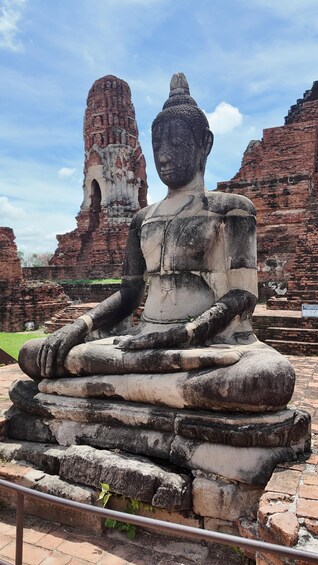 A large stone Buddha statue in a historical site with ancient brick structures in the background. 2