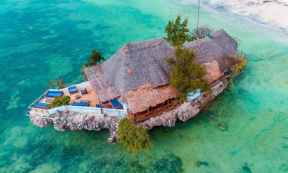 An aerial view of a secluded island with thatched-roof structures and clear turquoise waters. 2