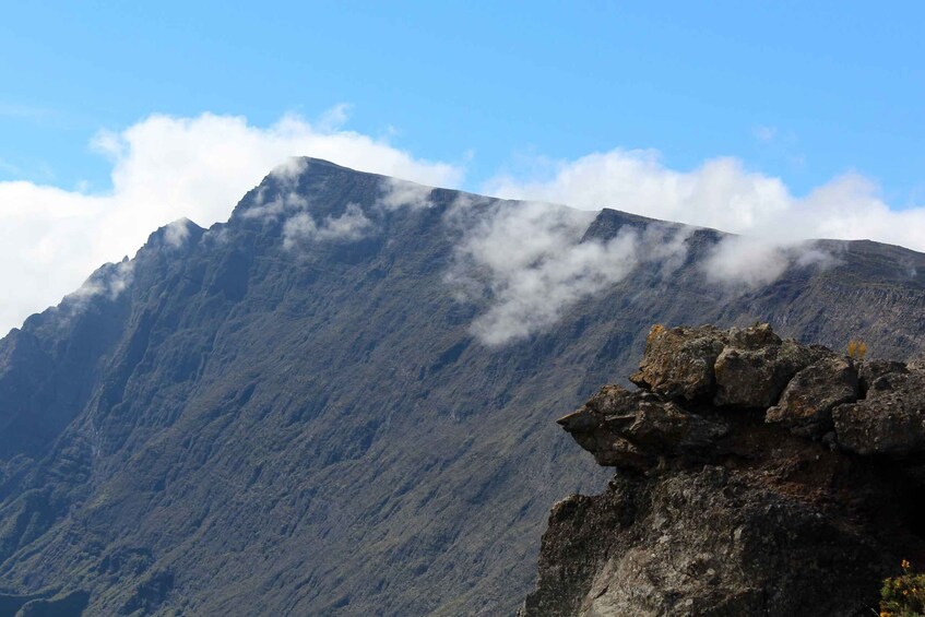A mountain with a rocky outcrop in the foreground and clouds at the peak. 5